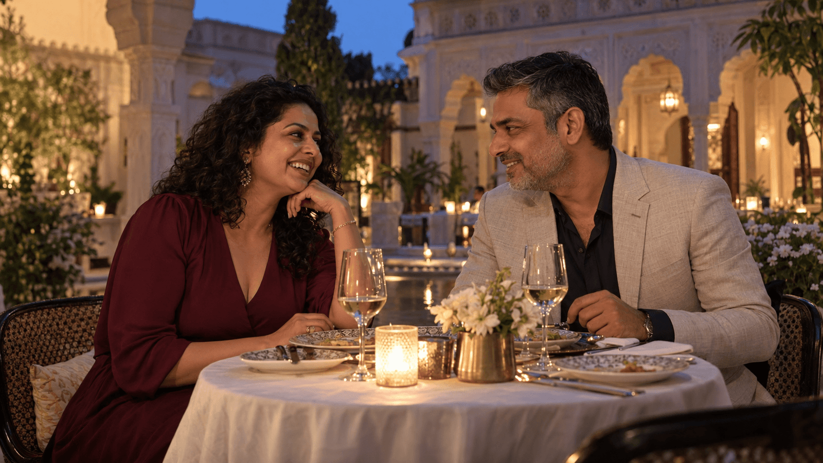 Two adults smiling at each other over dinner in a courtyard.